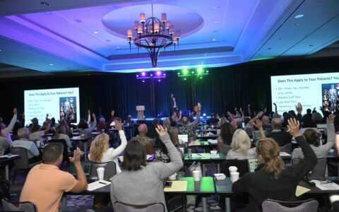 A crowd raises their hands while Dr. Albano asks a question on stage at the 2025 Worldlink Medical Summit